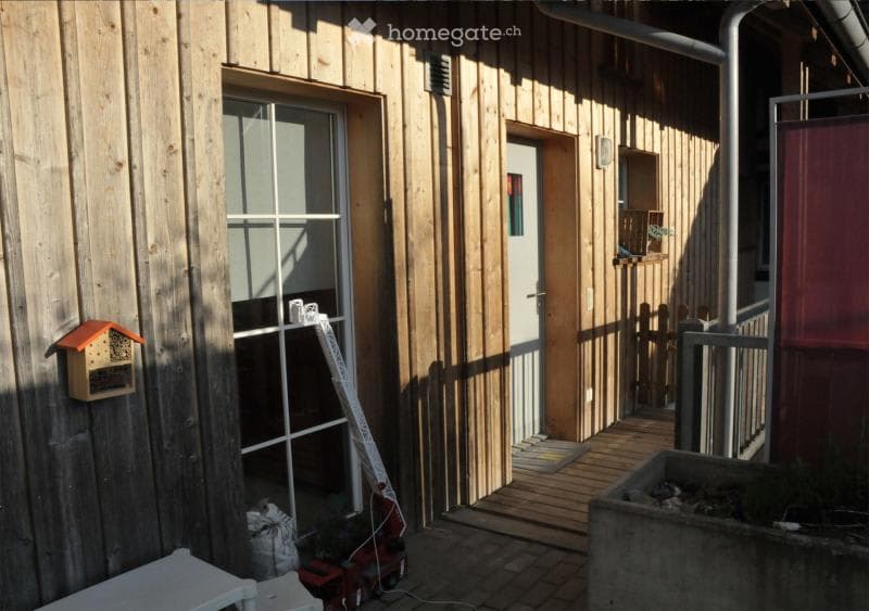 exterior of house with wooden wall, wooden door, glass window, small balcony, bee house on the wall, wooden deck with fence