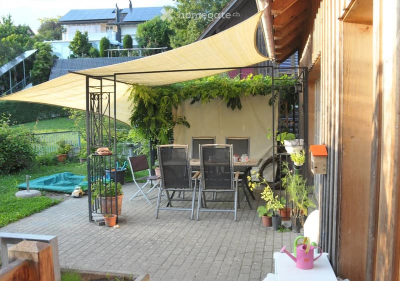 a table with chairs, potted plants, a watering can, and a yellow canopy