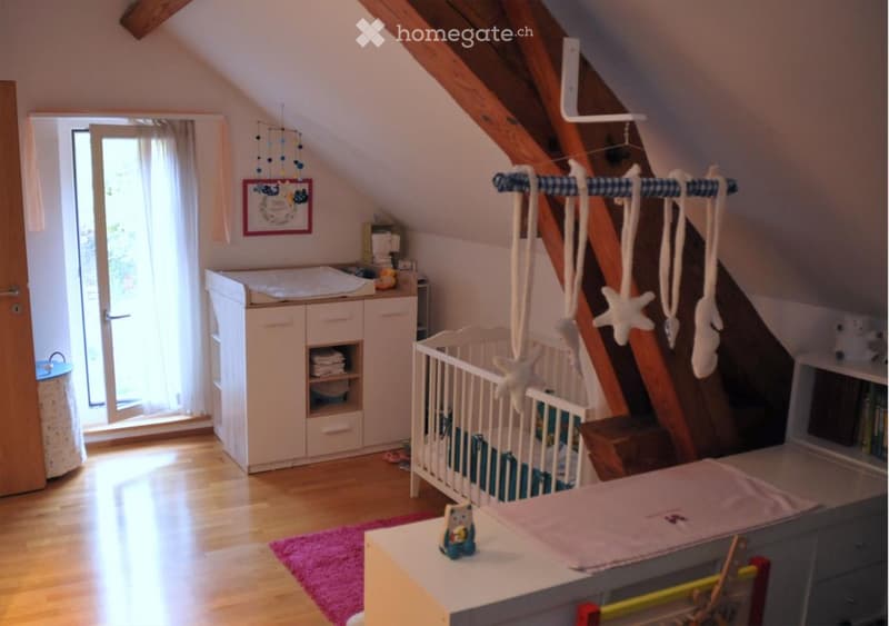 A nursery with crib, wooden beams, wooden floor, crib mattress, white cabinets, wooden door, pink rug, picture frame, play gym