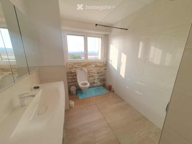 modern bathroom with white tiles, wooden floor, glass-enclosed shower, sink, toilet, window, mirror, rug