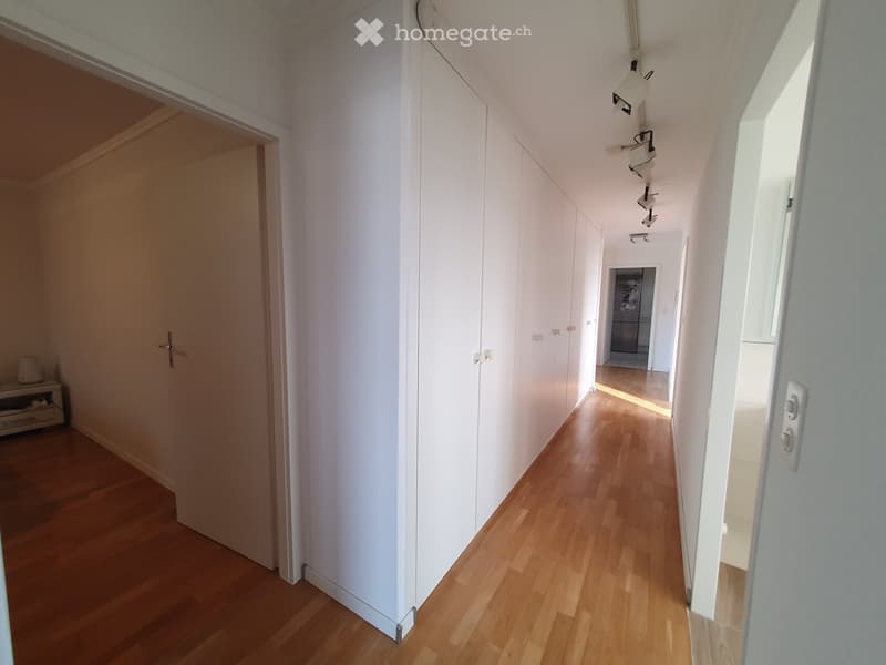 a hallway with wooden flooring, white cabinets, and ceiling lights