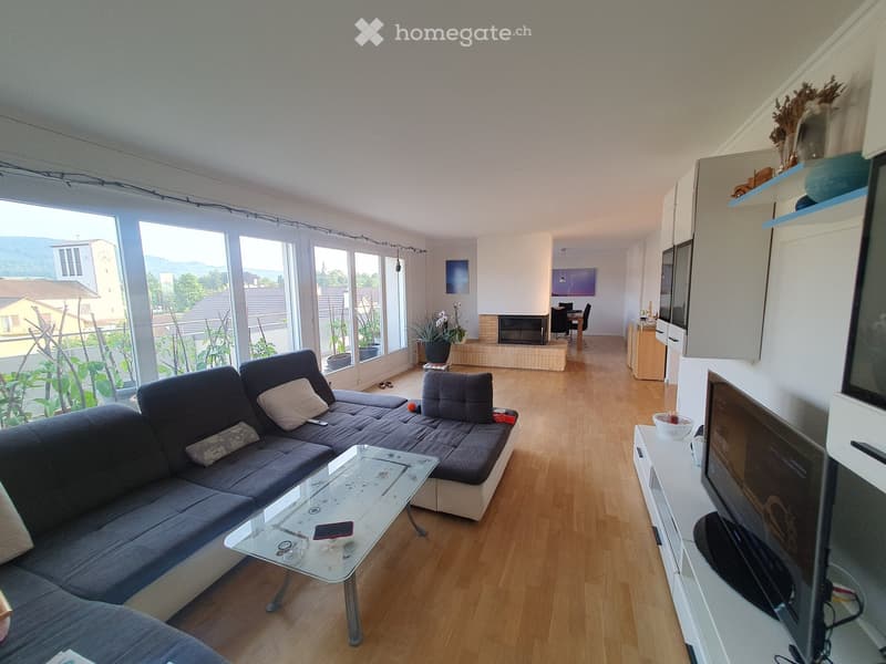 large windows, wooden floor, two sofas, glass table, two televisions, large fireplace