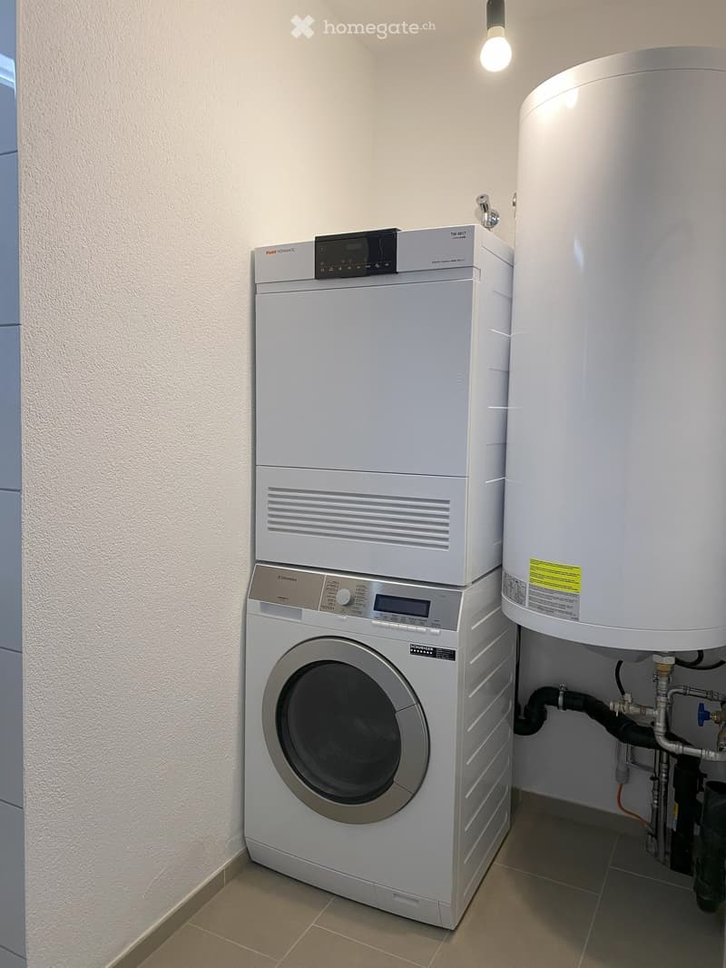 A small laundry room with a stackable washer and dryer, and a hot water tank.