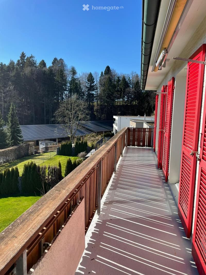 large balcony with wooden railing, red shutters, view of greenery and trees
