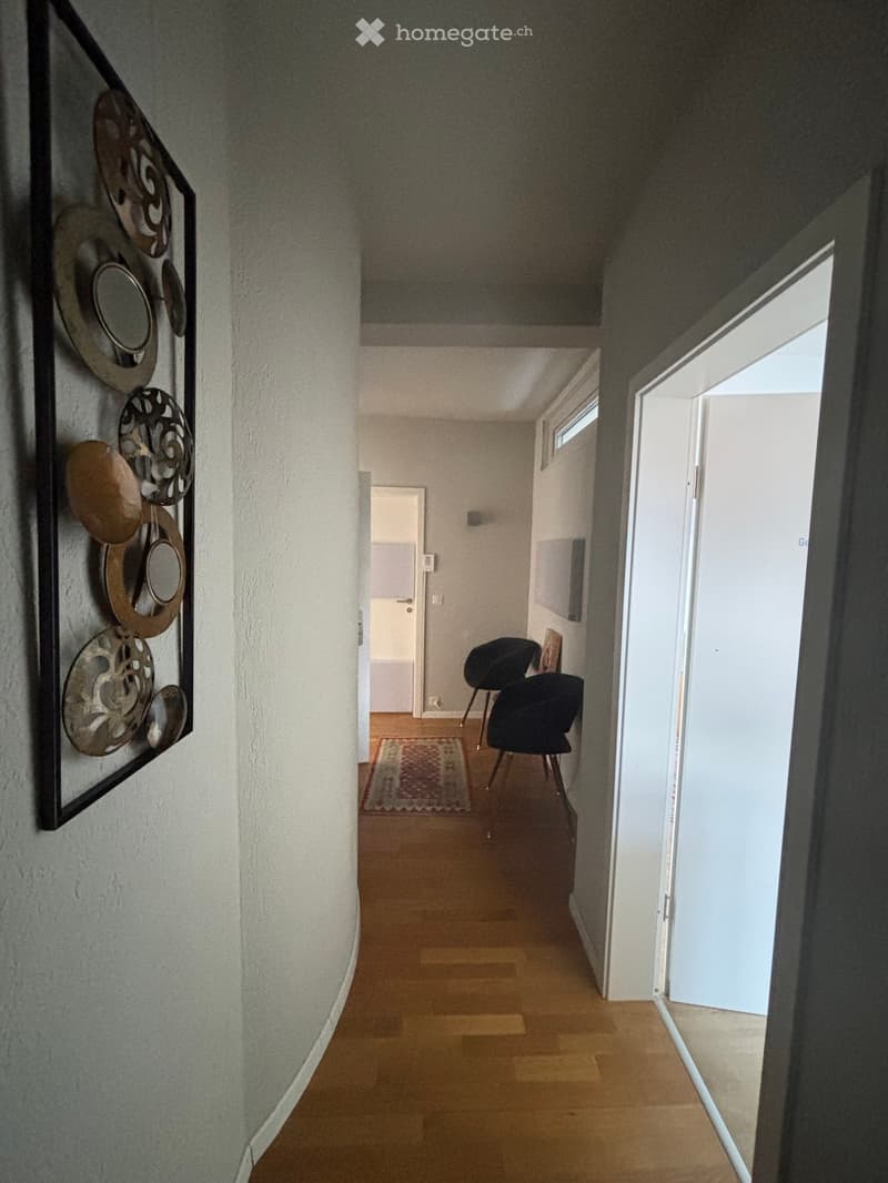 A curved hallway with a wall decoration, wooden flooring, and an open doorway leading to a door.