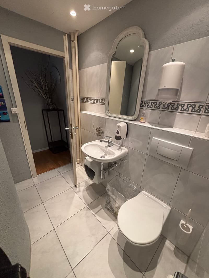 white tile flooring, white sink, white toilet, mirror, wall mounted soap dispenser, wall mounted tissue dispenser