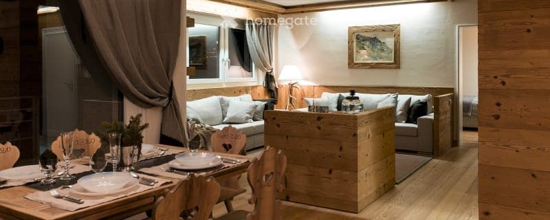 Cozy wooden interior, dining table, sofa, fireplace, wooden counter, white plates, wine glasses, wooden chairs, artwork, lamps
