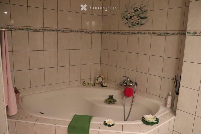 bathroom with corner bathtub, beige tiles, hanging towel, decorative flowers, small shelf