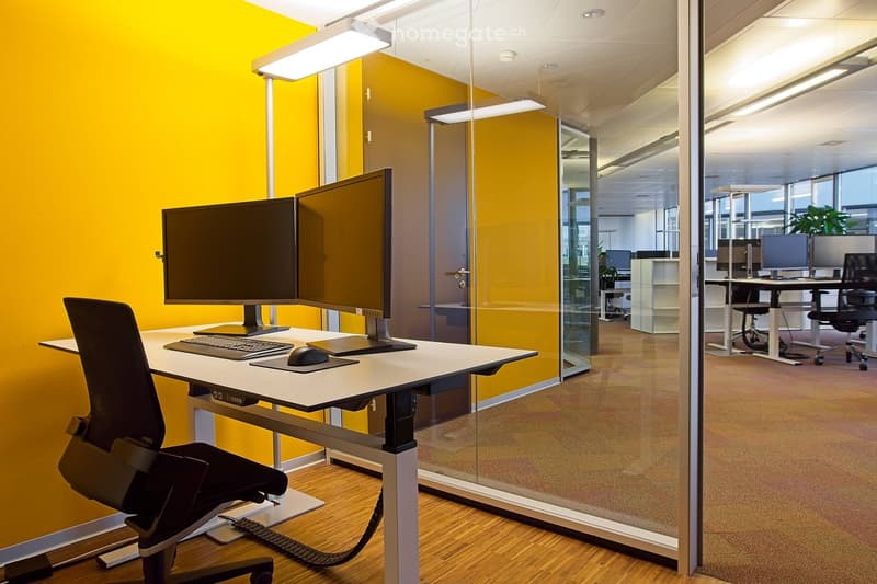 Office with sit-stand desk, black chair, two monitors, yellow walls, and modern interior.