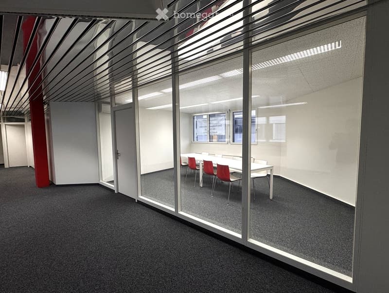 large open room, glass walls, gray flooring, conference table with chairs