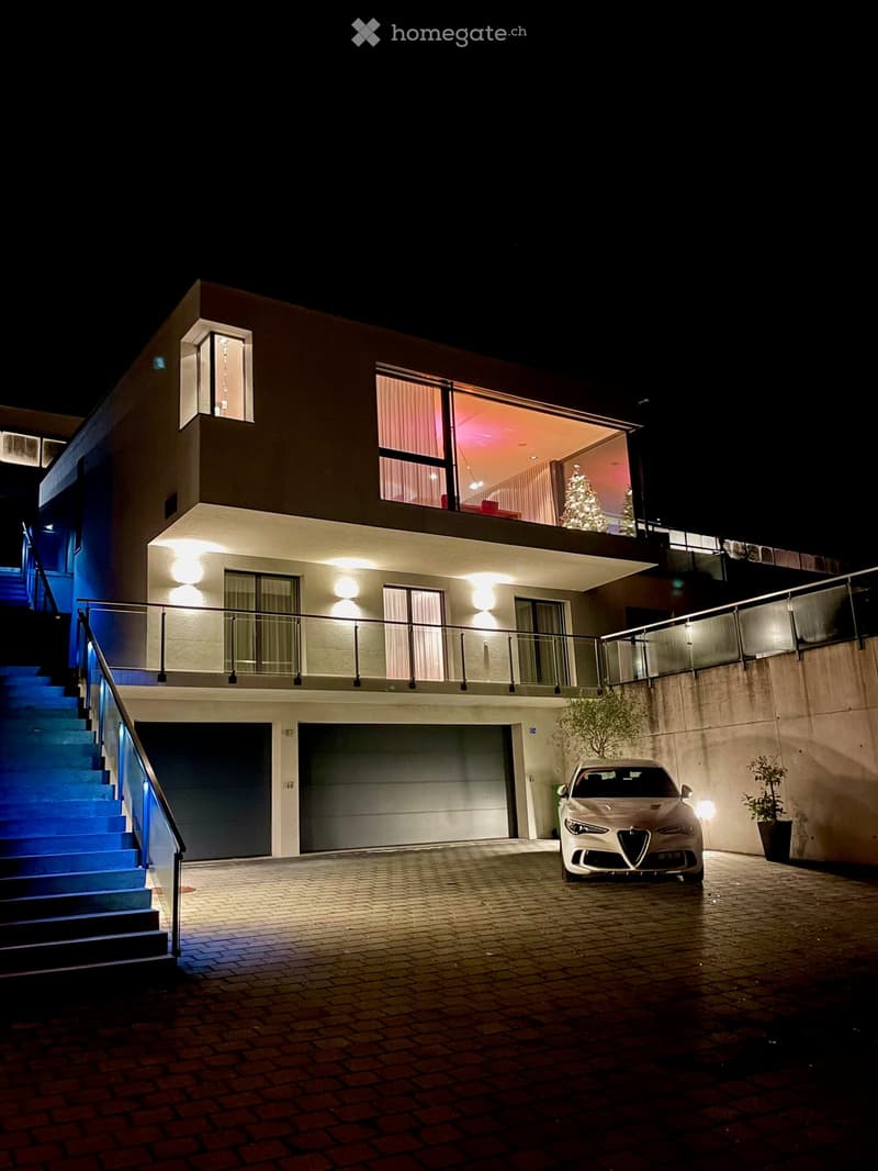 Modern 2-story house, well-lit, car parked in front, blue steps, garage with 2 doors, decorated with Christmas tree