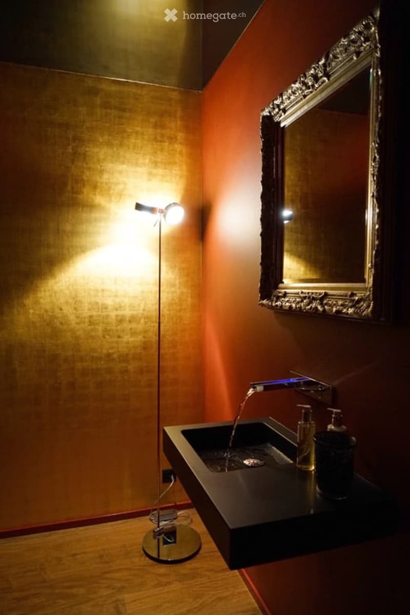 a bathroom with red walls, a golden-textured wall, a mirror, a sink, and a lamp