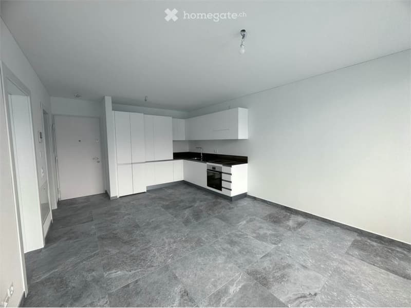 Empty kitchen with white cabinets, gray marble flooring, and a central island with built-in appliances.