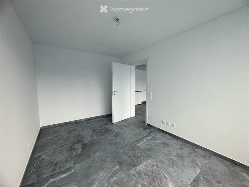 Empty room with tiled floor, white walls, open door, power outlets on wall.