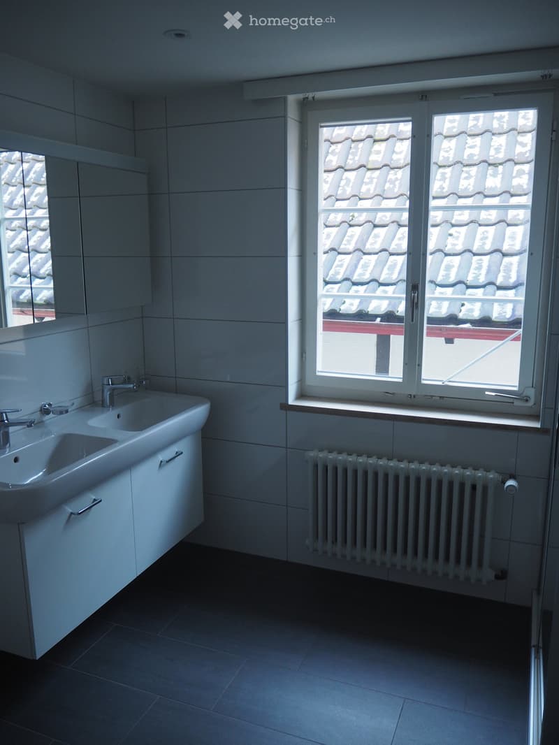 White double sink with cabinets, white tile walls, white tiled floor, window with view to the roof