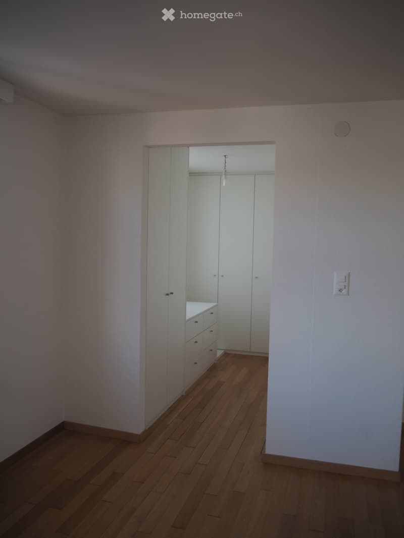 Empty room with white walls and wooden floors, large wardrobes, mirror on the wall, white cabinet with drawers.