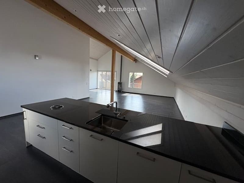 Modern kitchen with a sink, black countertops, white cabinets, wooden beams, and a ceiling lamp.