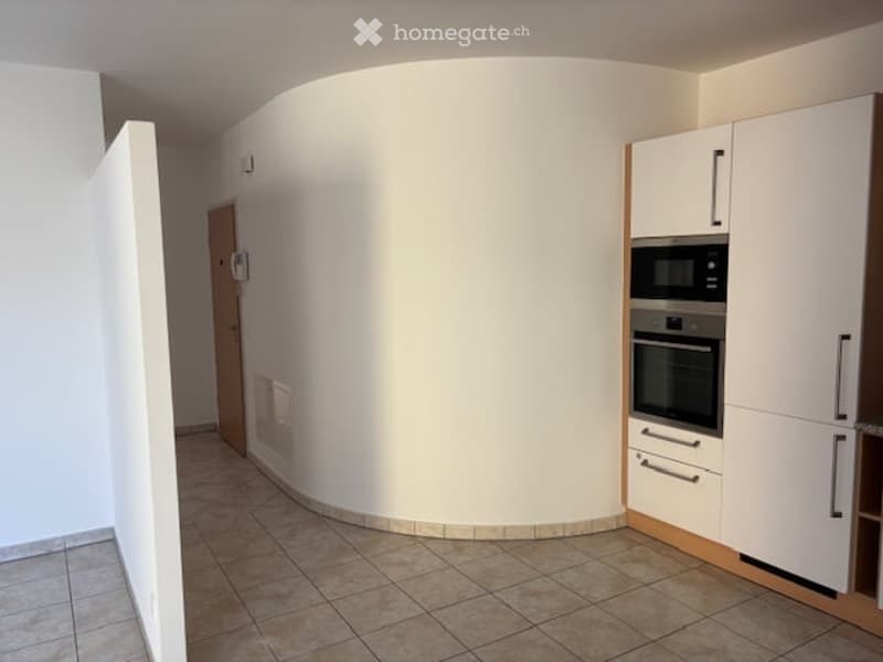 Empty room with white walls, tiled floor, built-in oven and microwave, wooden door, white cabinets