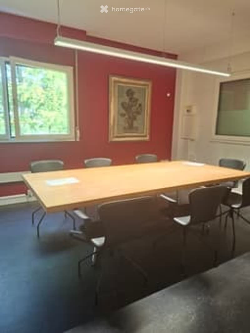 empty meeting room with long wooden table, red walls, white ceiling, glass windows