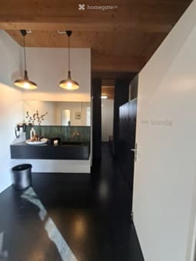 modern bathroom with white walls, black floor, wooden ceiling, mirror, white sink, black countertop, two lamps