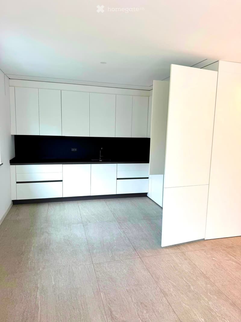 Empty kitchen with white cabinets, black countertop, and light grey tiled floor.
