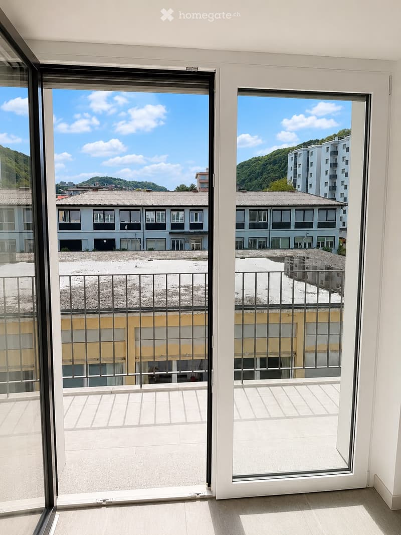 Balcony with large glass doors opening to a tiled balcony area, overlooking a cityscape with buildings and a hillside.