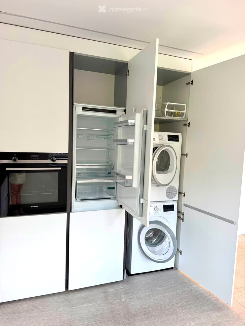 Compact kitchen area with a refrigerator, oven, and washing machine, all integrated into white cabinetry.