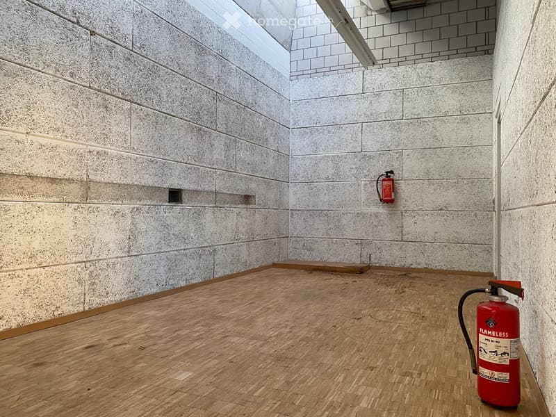 Empty room with wooden floor, concrete walls, and two fire extinguishers