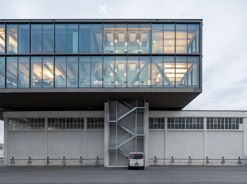 modern design building with glass exterior, large windows, steel staircase, metal railings, large white walls, charging points with bicycles, white van parked