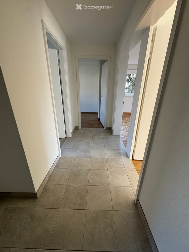 An empty hallway with tiled flooring, white walls, and wooden floors in the rooms