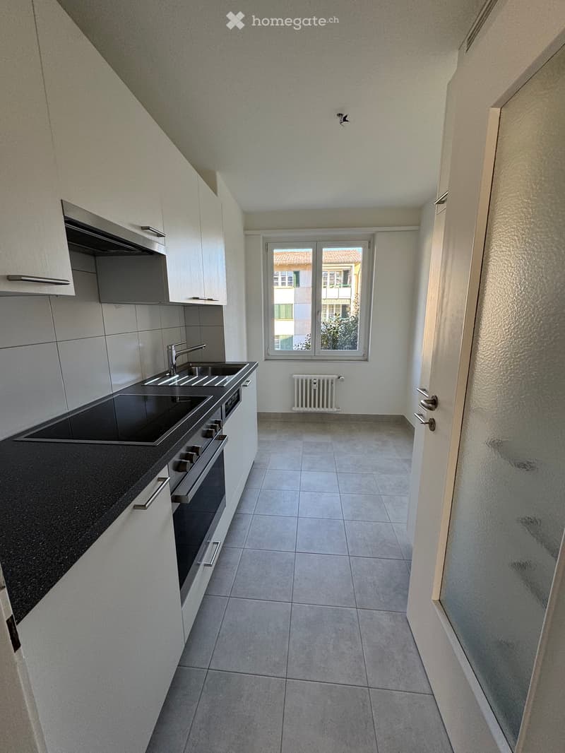 Modern kitchen with white cabinetry, black countertops, double oven, granite countertops, windows with view