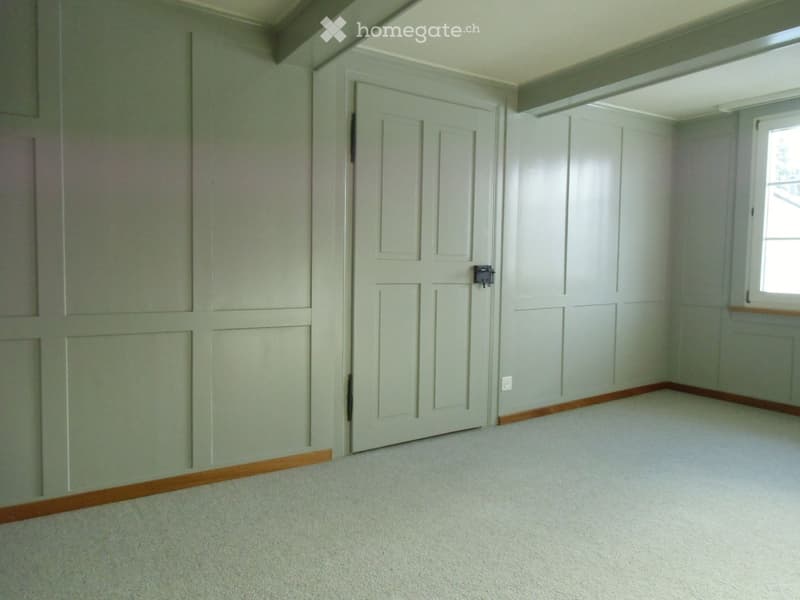 Empty room with white walls and floor, wooden panels on walls, white door, power outlet.