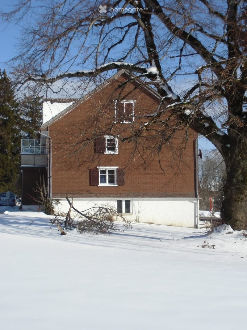 2 story house, brown brick, white windows, balcony, garage, trees, snow