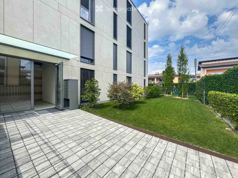 modern building, glass entrance door, small patio area, neatly trimmed grass, shrubs, trees, outdoor playground equipment