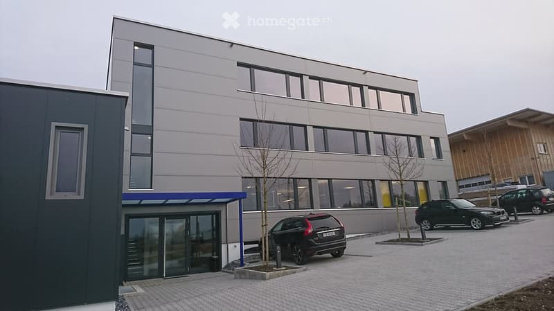 modern building, grey and white facade, large windows, glass doors, paved parking area, two cars parked
