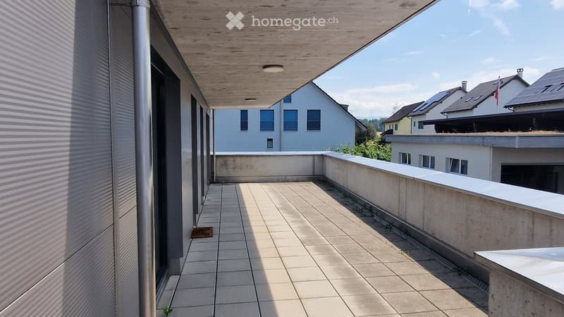 Balcony with tiled floor, low concrete railing, and wooden ceiling, overlooking neighboring buildings.