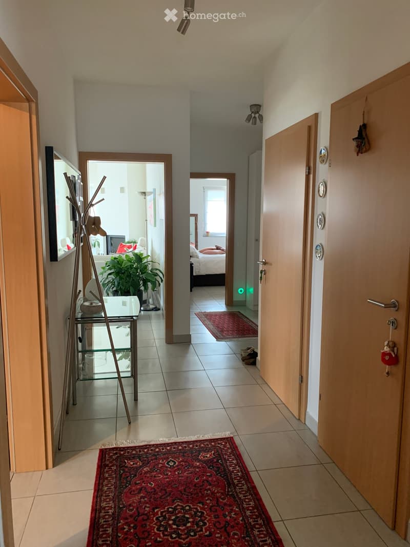 long hallway, white tiles, wooden doors, coat rack, potted plant, carpet, shoes by the door