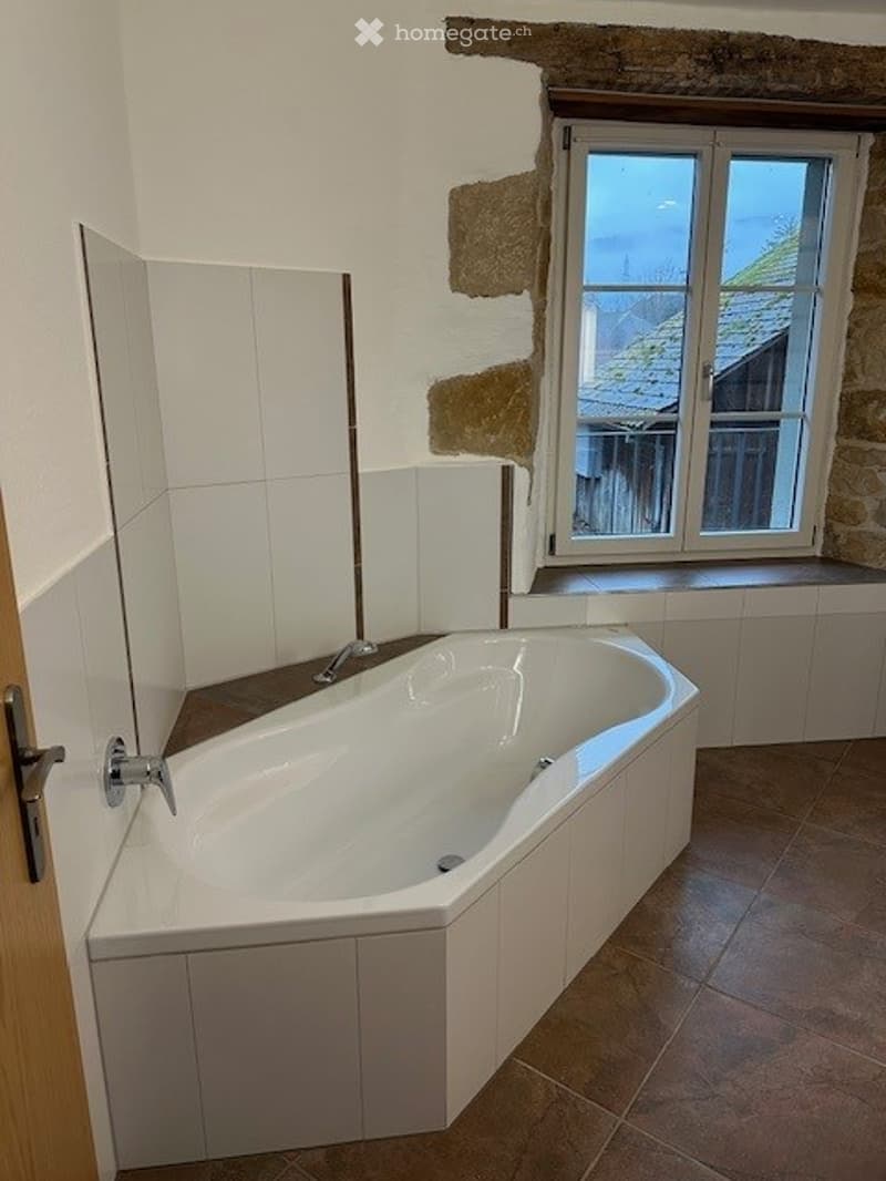 A modern bathroom with a bathtub, white tiles, brown tiles, a window, and a faucet