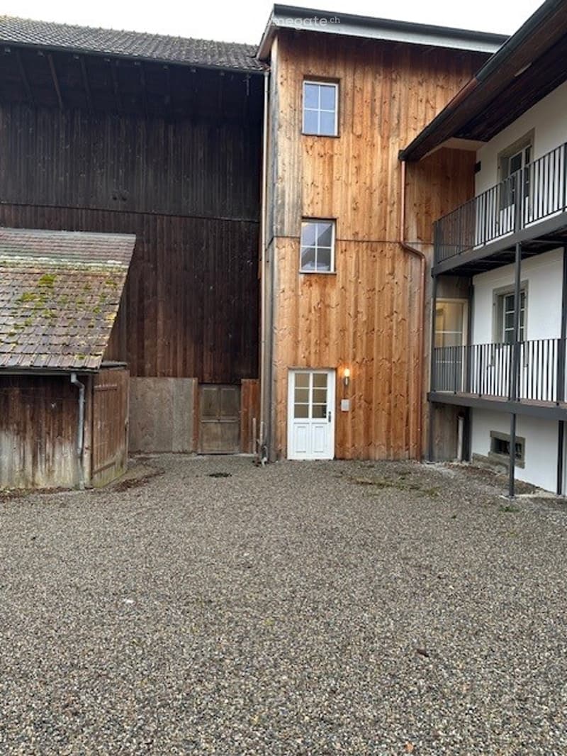 two buildings with balconies, gravel parking lot, wooden doors, a building with a sloped roof and moss