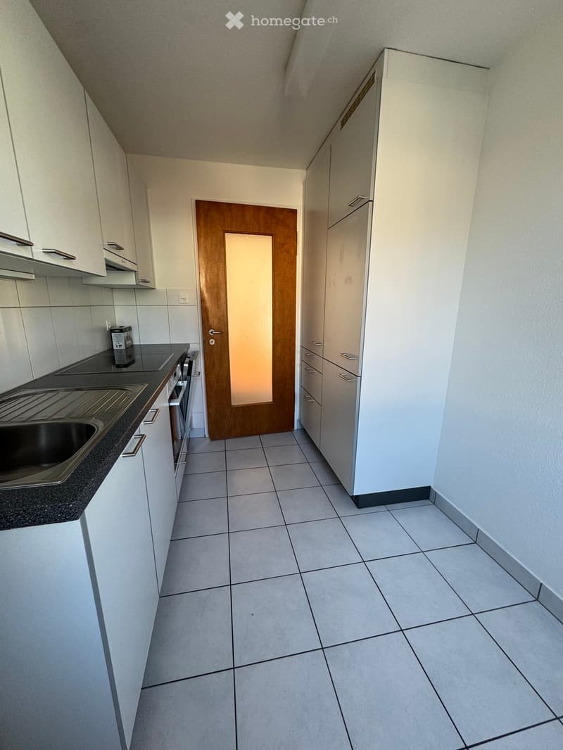 empty kitchen with tiled floor, wooden door, stainless steel sink, granite countertop, white cabinets, built-in dishwasher and washing machine