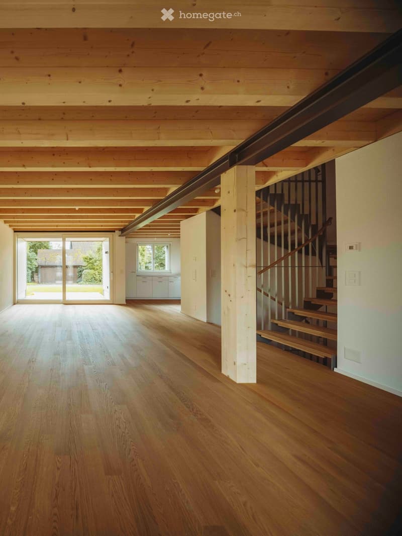 Open floor plan with large glass sliding door leading to the garden, wooden ceiling beams, and hardwood flooring.