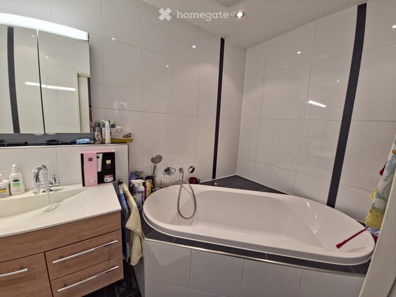 large bathtub, white tiles, wooden cabinets, mirror, white countertop, sink, shower head