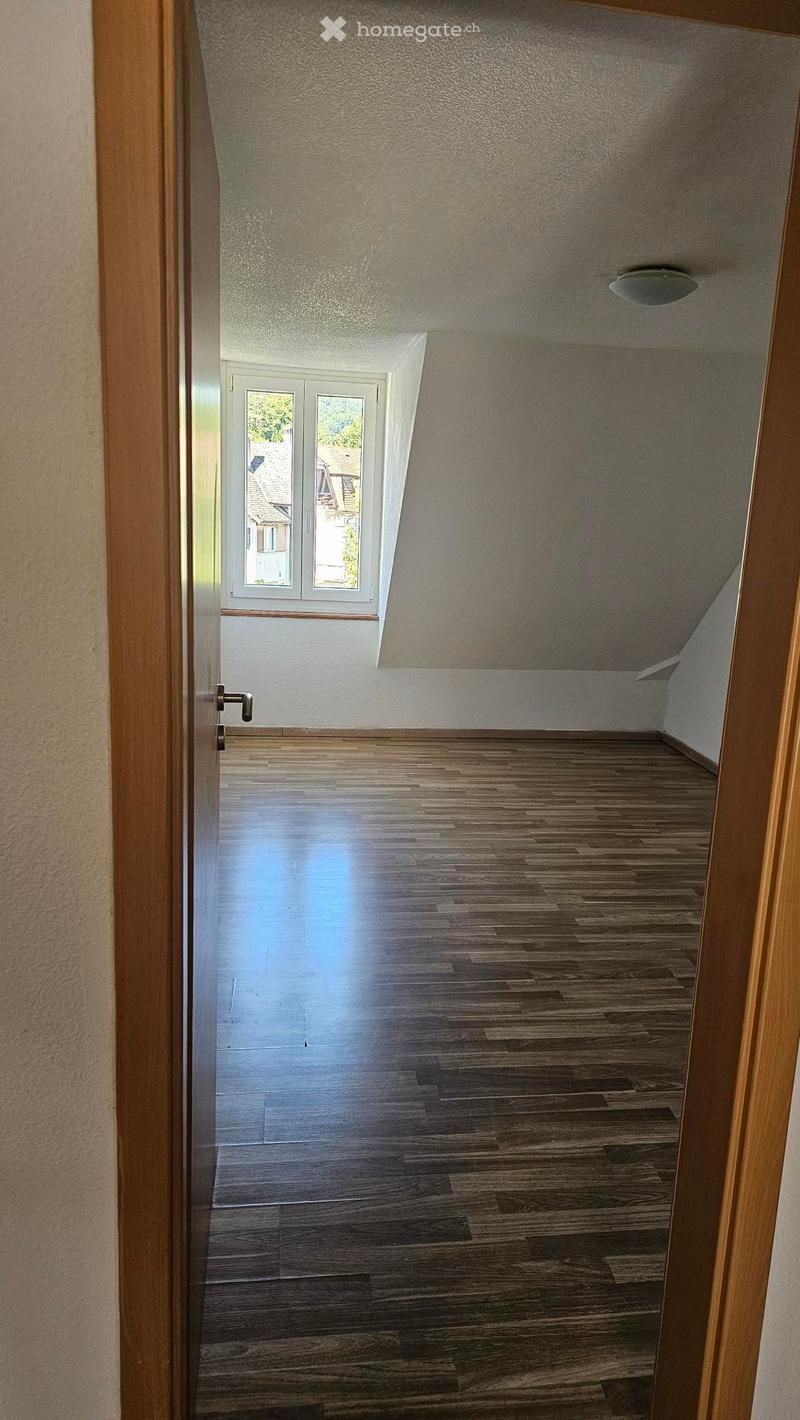 Empty room with wooden floors and white walls. There is a window and a ceiling light.