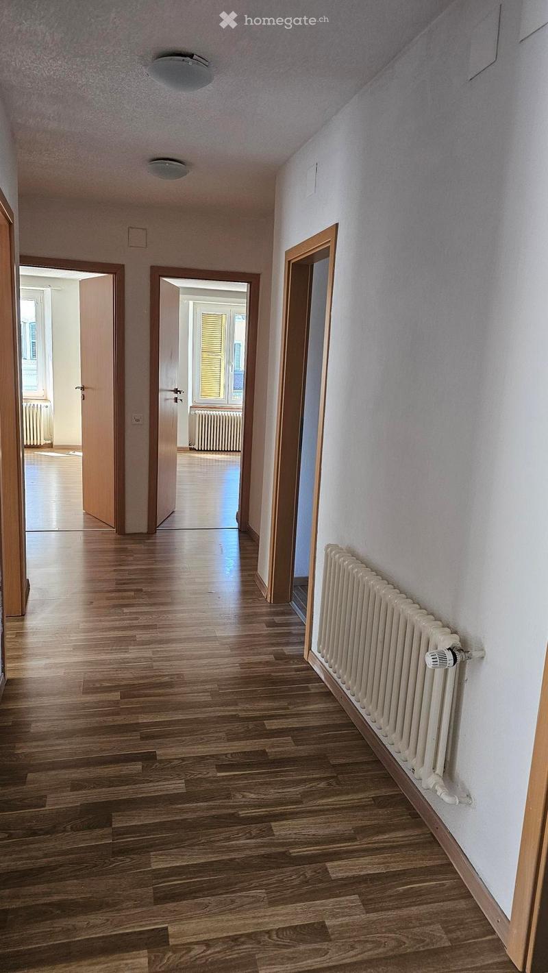 Hardwood floor, white walls, 3 open doors, radiators, open rooms with windows.
