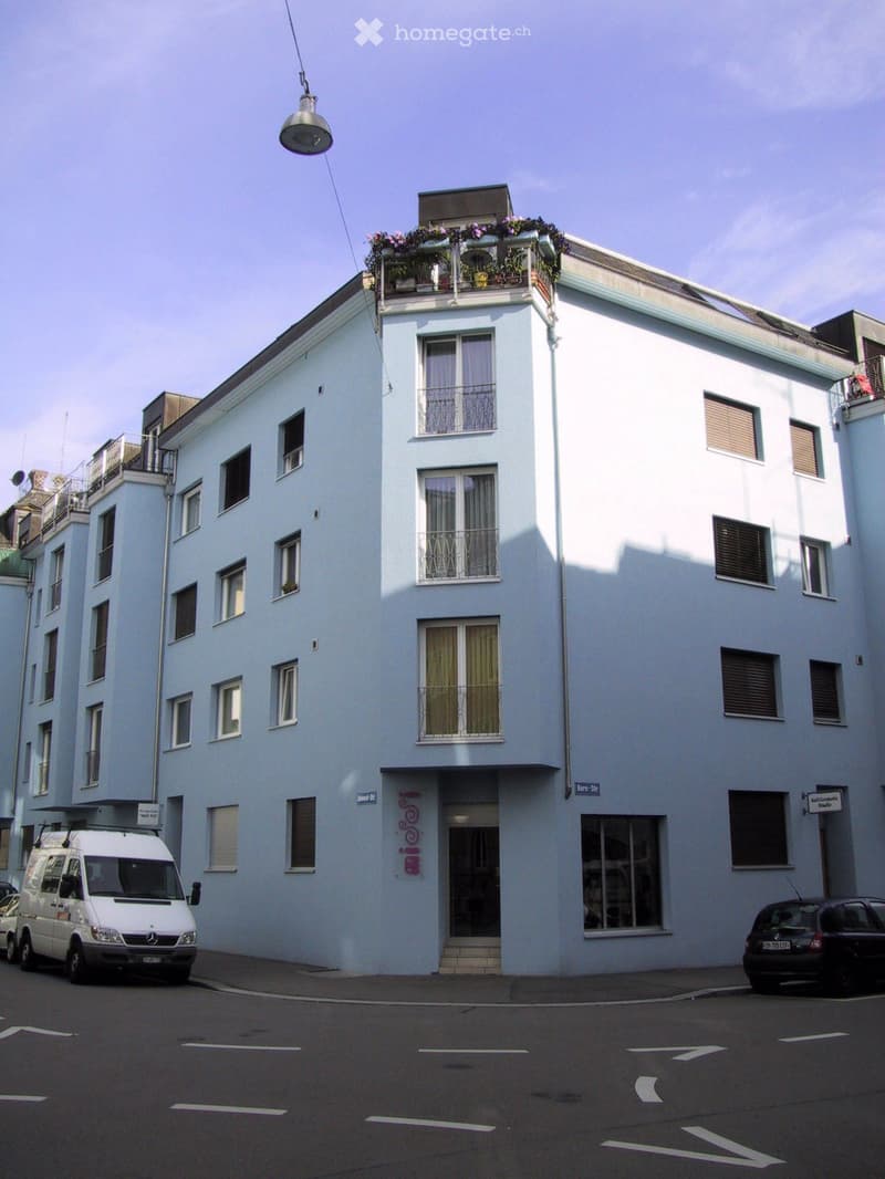 5 story building, light blue exterior, multiple balconies, windows with shutters, entrance on the ground floor