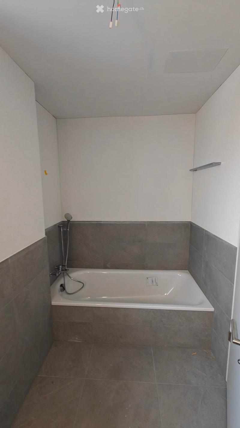 Bathroom with a bathtub, gray tiled floor and walls, shower head attached to wall, no furniture