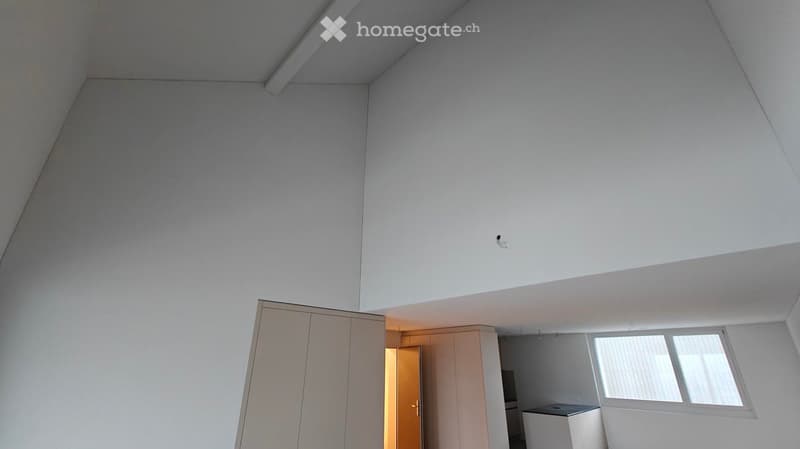 Empty room with white walls, ceiling, and floor. There is a large wardrobe and a small cabinet. There is a window with blinds.