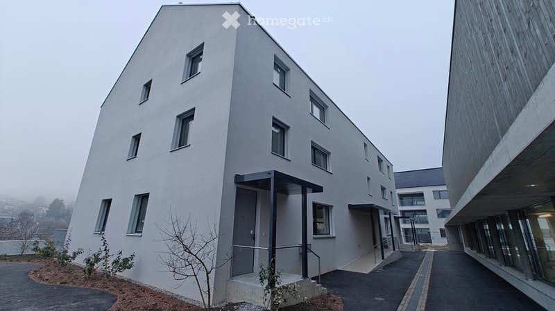 Modern apartment building with white exterior walls, large windows, black canopy, grey driveway