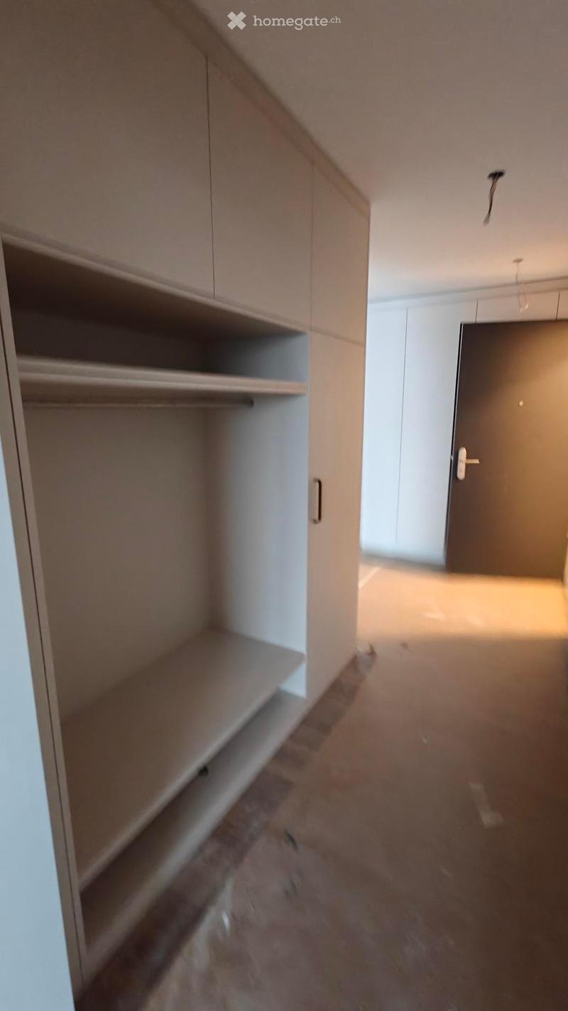 Empty room with built-in wardrobes, wooden floor, white walls, and a door.
