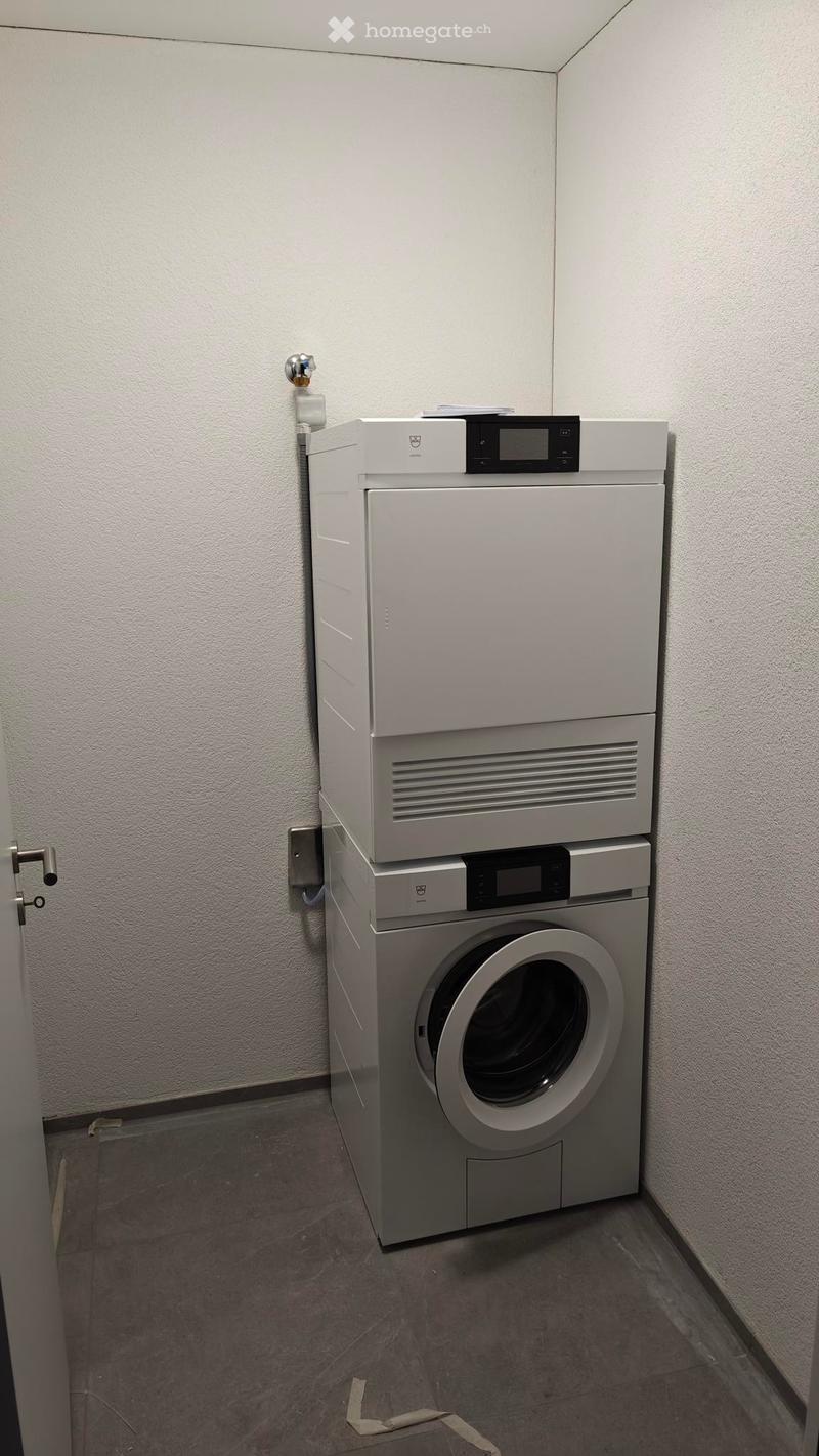 A room with a white washing machine and a white dishwasher stacked on top of each other against a white wall.